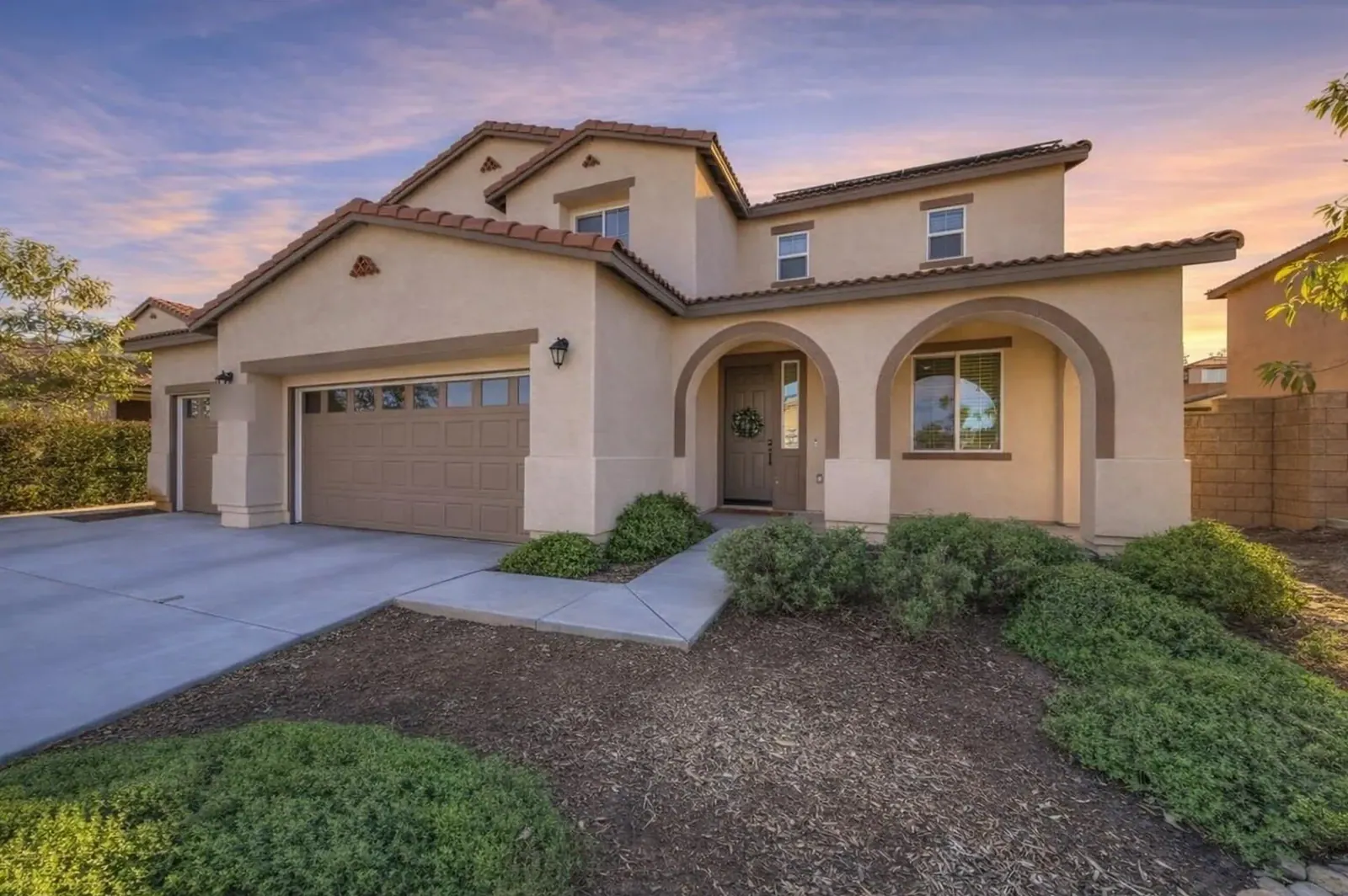 Stucco two-story with arched porch under a sunset sky