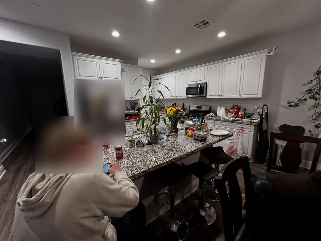 Original iPhone photo of a lived-in kitchen with a person at the island (face blurred)